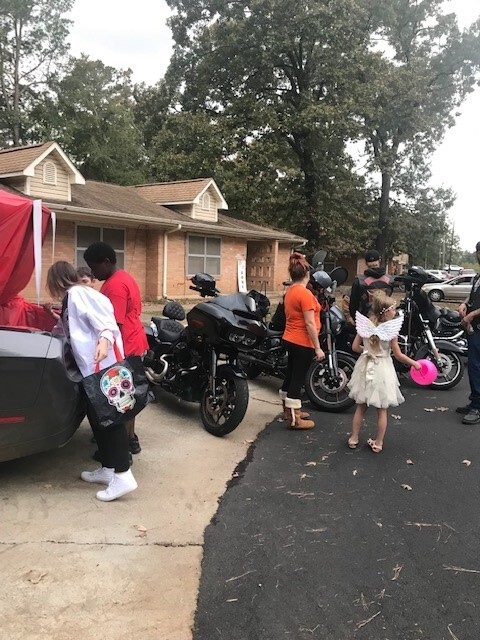 Group of individuals outside looking in trunk and standing by motorcycles.