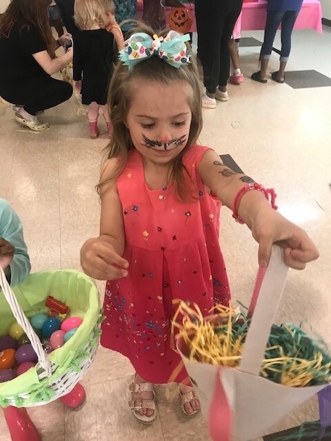 One girl holding up a basket filled with Easter grass and eggs.