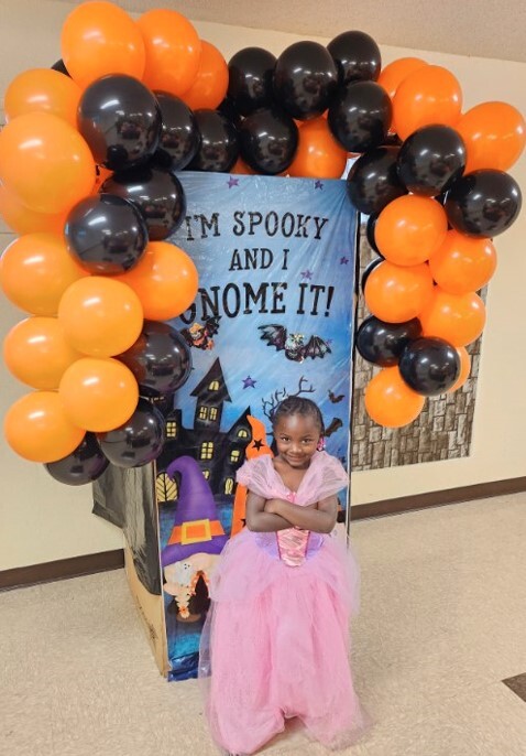 A princess standing in front of the halloween sign surrounded by balloons.