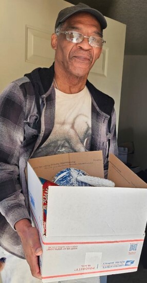 A man standing in his doorway holding a box from the Christmas food giveaway.