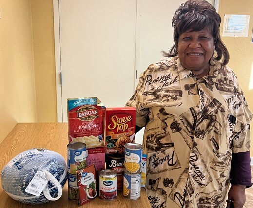 A woman standing by a table with the contents of a box from the Christmas food giveaway on it.